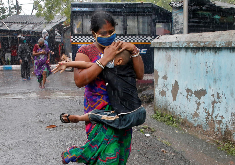 A woman carries her son as she tries to protect him from heavy rain while they rush to a safer place, following their evacuation from a slum area before cyclone Amphan makes its landfall in Kolkata on May 20, 2020. REUTERS/Rupak De Chowdhuri
