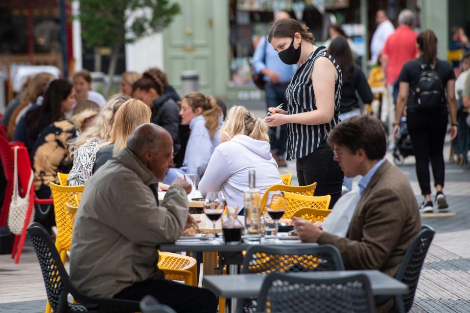 File photo dated 29/06/21 of a waitress wearing a face covering serving diners at outside tables in Kensington, London. (PA Wire)