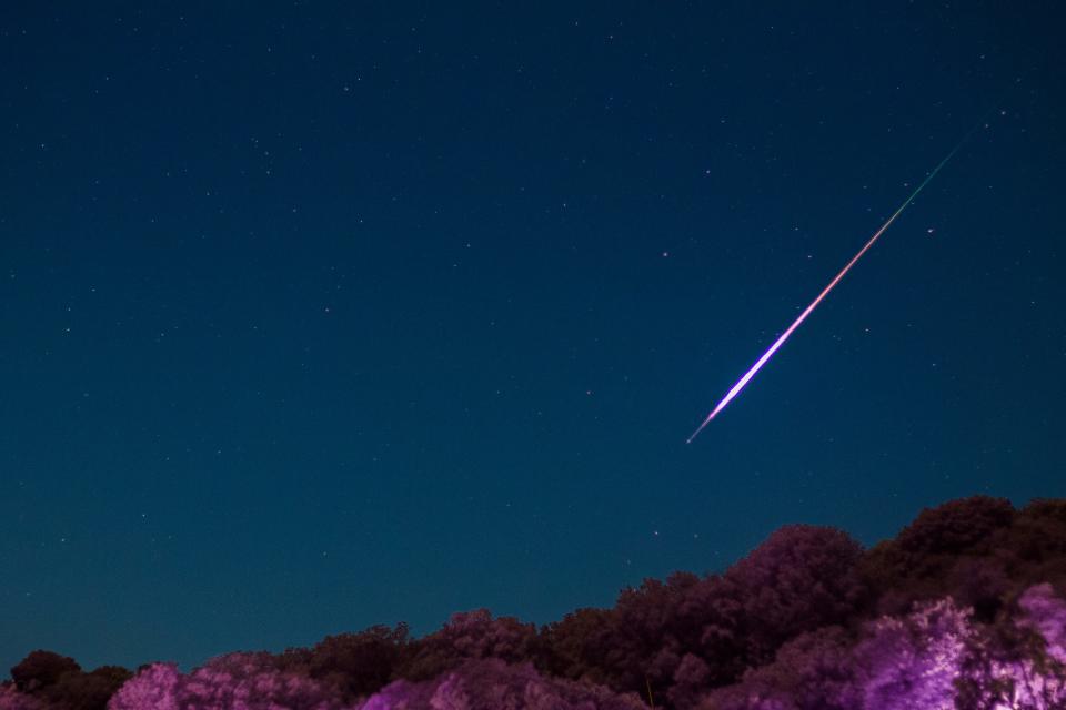 A bright purple meteor streaks across the night sky
