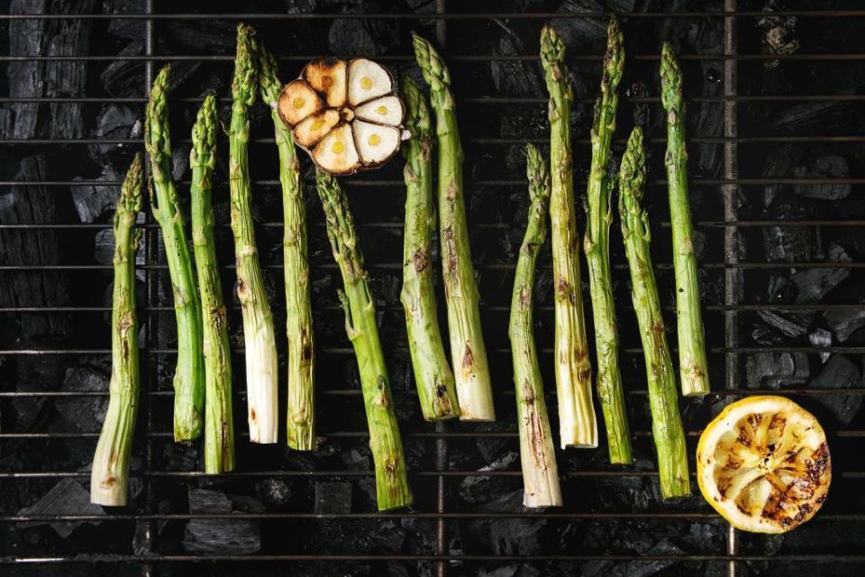 grilled vegetables green asparagus, garlic, lemon on bbq grill rack over charcoal top view, space