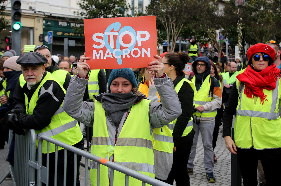 A demonstrator wearing her yellow vest holds a placard during a visit by French Foreign Minister Jean-Yves Le Drian in Biarritz, southwestern France, Tuesday, Dec. 18, 2018. Yellow vest protesters occupied dozens of traffic roundabouts across France even as their movement for economic justice appeared to be losing momentum on the fifth straight weekend of protests. (AP Photo/Bob Edme)