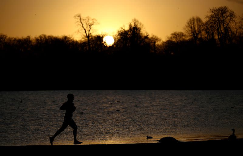 FILE PHOTO: A man jogs past the Round Pond in Kensington Palace Gardens as the sun rises in London