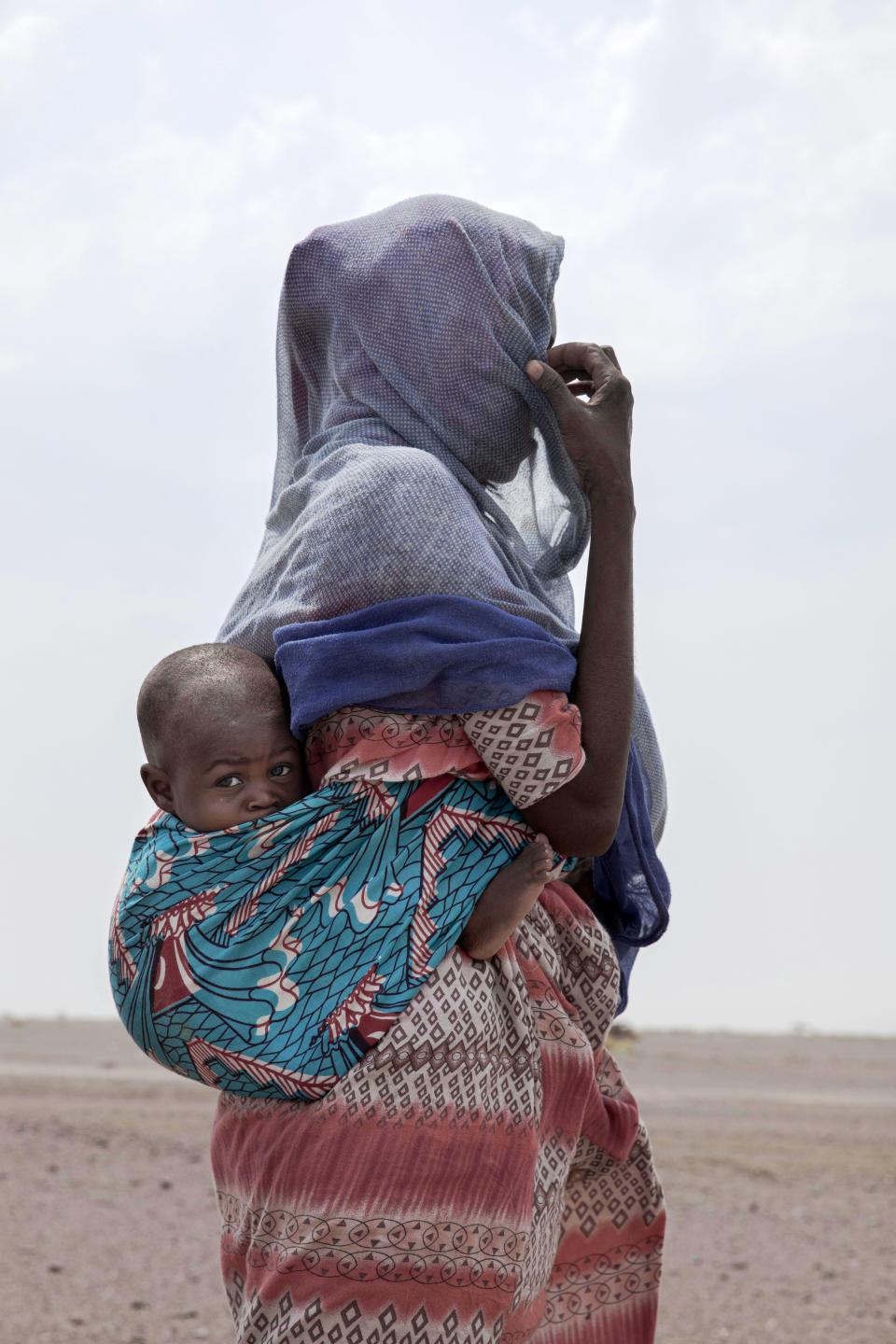 In this July 23, 2019 photo, Fatma, a migrant from Mali, carries her one-year-old Said Yaacoub, as she makes her way in Lahj, Yemen. Mohammed, traveled with her husband, a construction worker, and two children through Djibouti on their way to Saudi. Once they reached the shore, they were held for several days by traffickers. (AP Photo/Nariman El-Mofty)