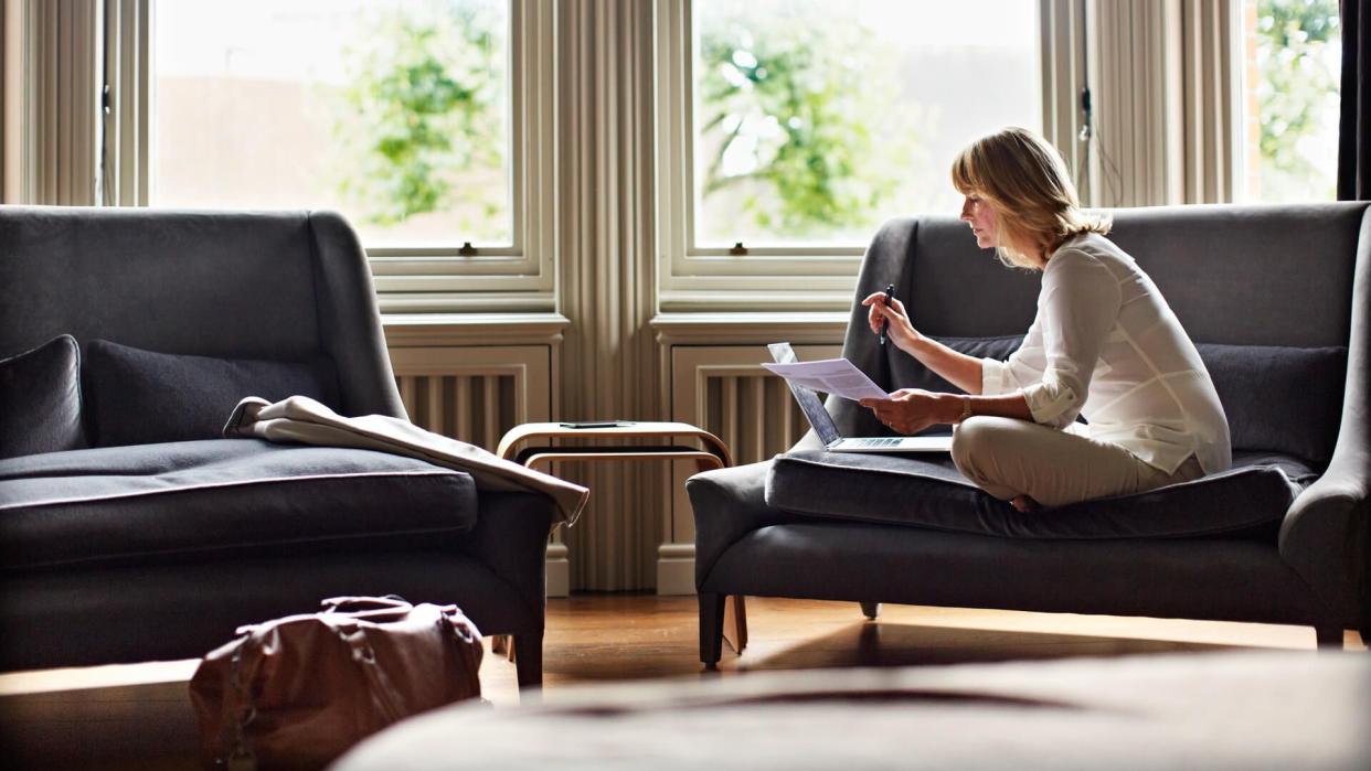 Shot of a mature woman working on a laptop in her living room after a trip.