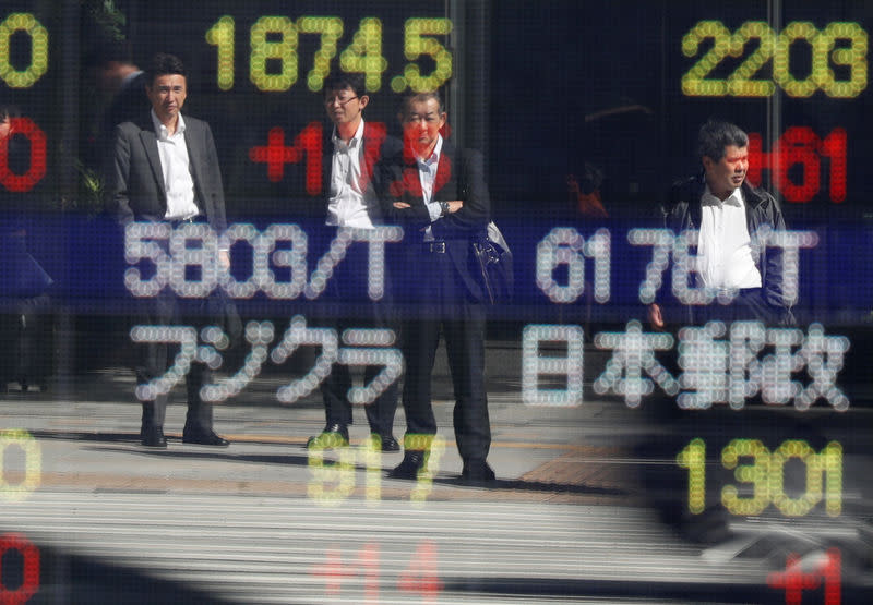 FILE PHOTO - Passersby are reflected in an electronic stock quotation board outside a brokerage in Tokyo, Japan, October 23, 2017. REUTERS/Issei Kato