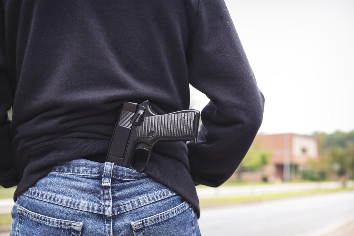 person's back with gun tucked into jeans facing school building
