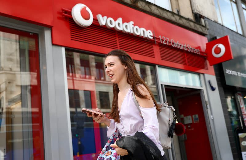 FILE PHOTO: A woman holds a phone as she passes a Vodafone store in London