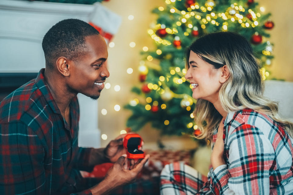 Young man surprising his girlfriend with engagement ring at Christmas