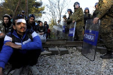 Migrants sit on the Greek side of the border with Macedonia as Macedonian policemen stand guard near the Macedonian town of Gevgelija, November 19, 2015. REUTERS/Alexandros Avramidis