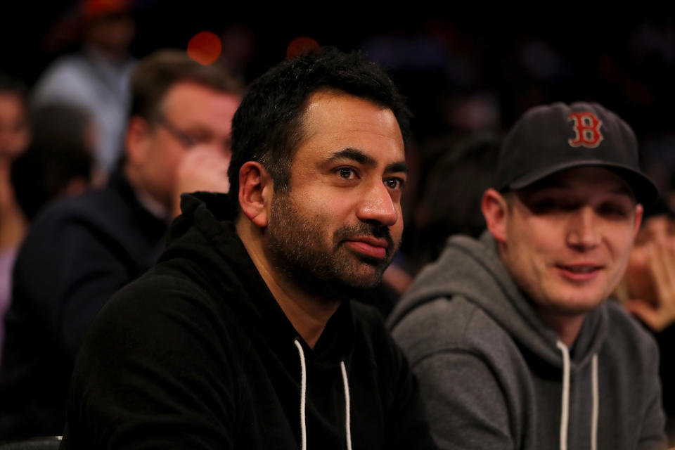 Kal Penn and a friend wearing casual hoodies are sitting courtside at a basketball game