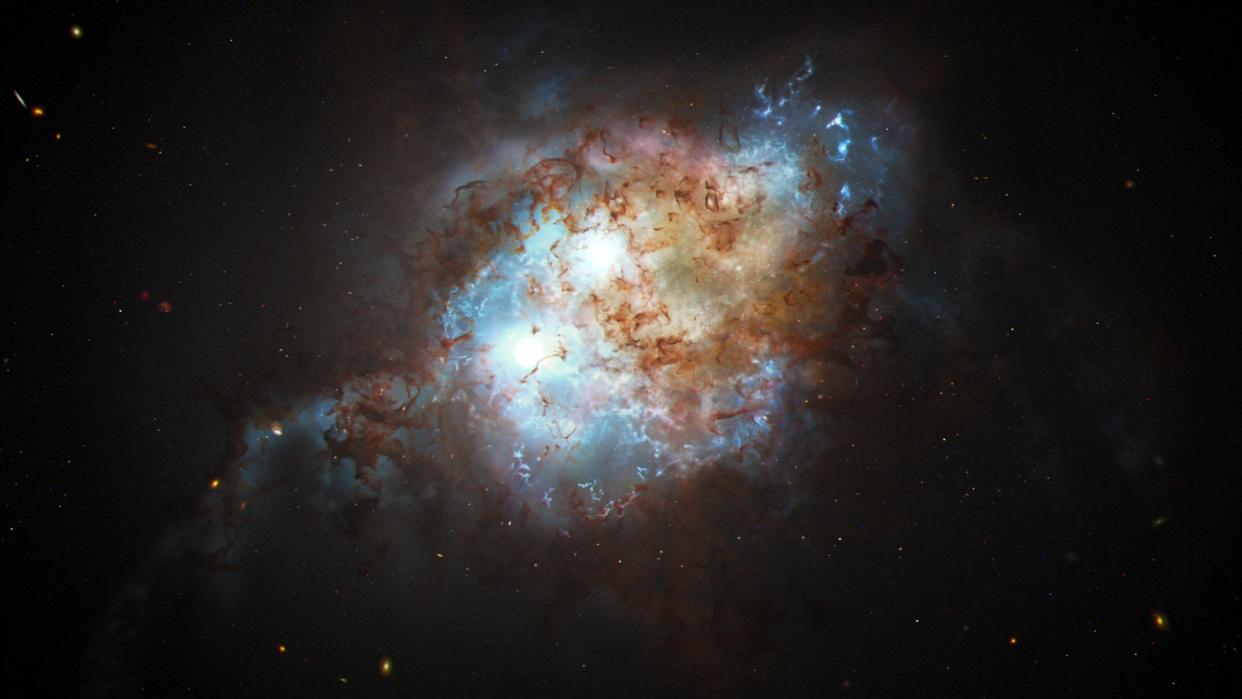  Two bright blue spheres representing supermassive black holes swirl amidst a cloud of blue and brown dust in the early universe 