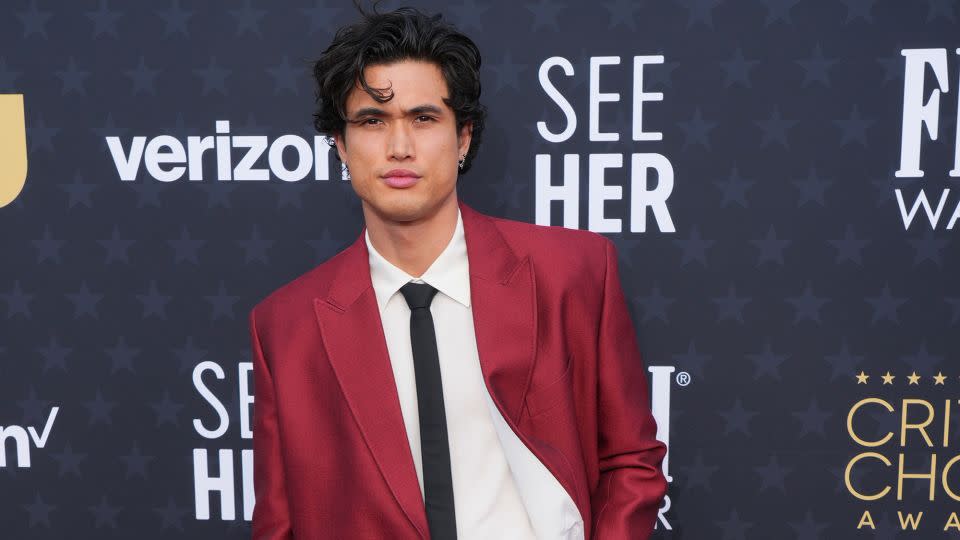 Charles Melton, nominated in the best supporting actor for his performance in "May December," wore a red Valentino suit paired with a black skinny tie featuring a V-shaped metallic accent. - Jordan Strauss/Invision/AP
