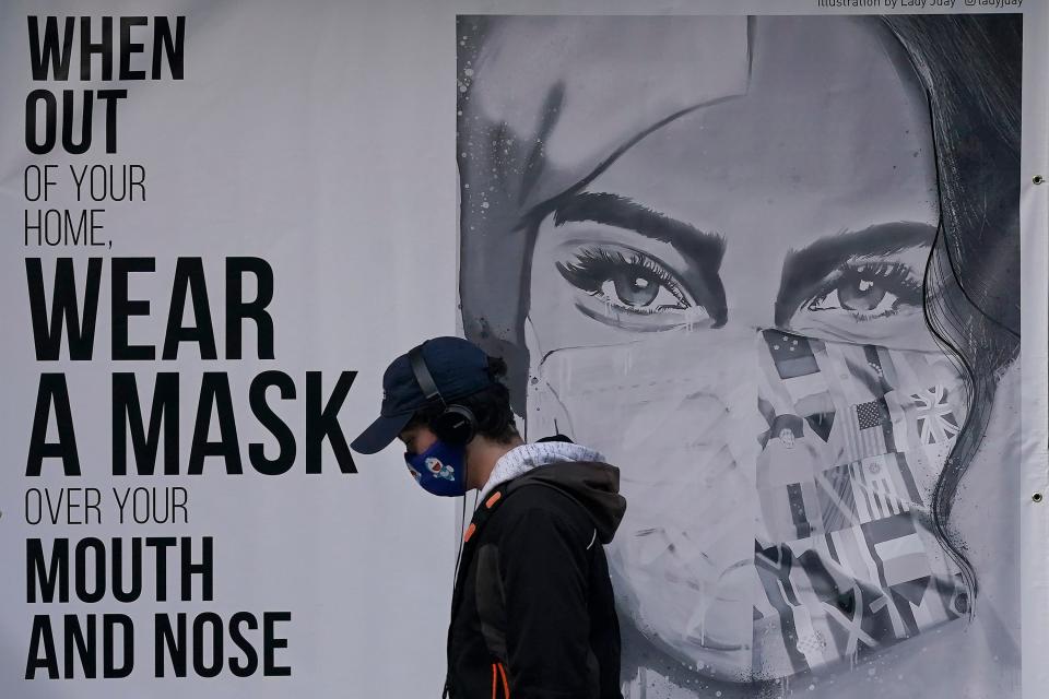 A pedestrian walks past a mural in San Francisco, which is joining a statewide curfew and Silicon Valley is banning all high school, collegiate and professional sports and imposing a quarantine for those traveling into the region from more than 150 miles away.