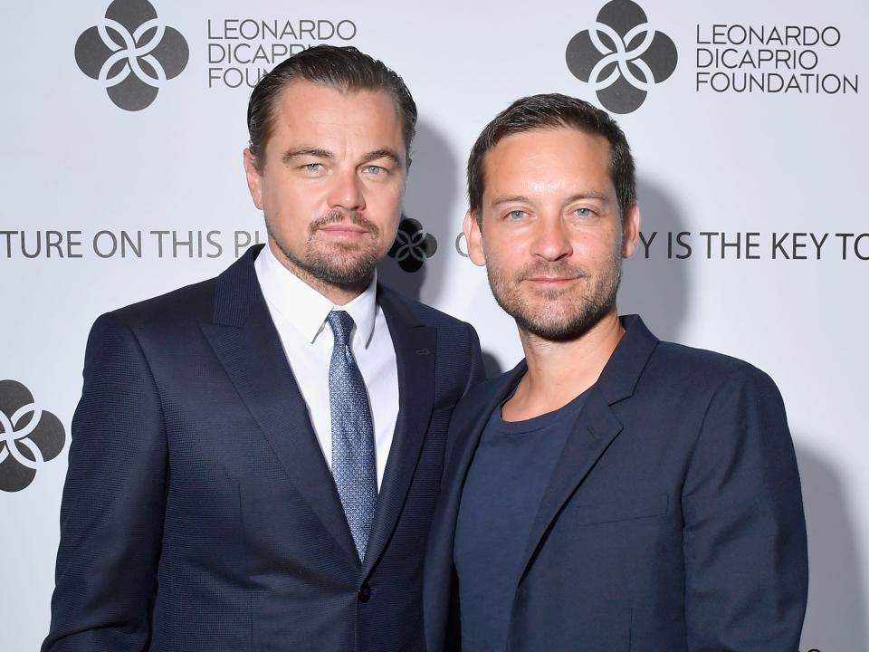 Leonardo smiling in a blue suit and tie and Tobey smiling in a blue shirt and blazer.