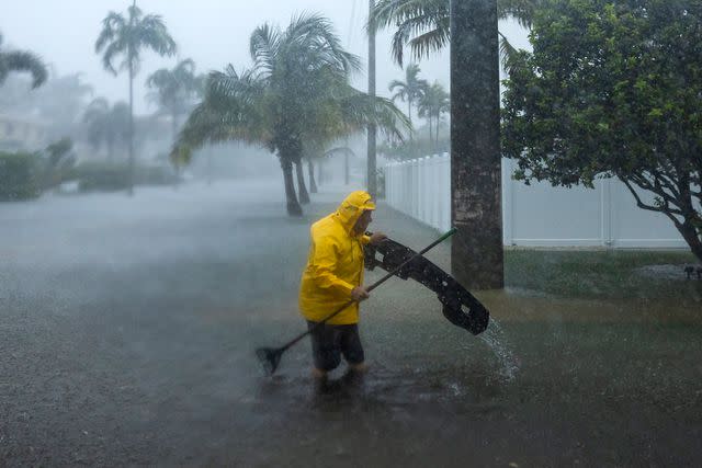 <p>Matias J. Ocner/Miami Herald via AP</p> A man works to clear debris from a flooded street in South Florida on Wednesday, June 12, 2024