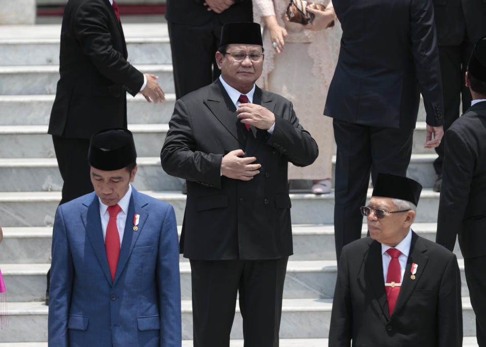 FILE - Newly inaugurated Defense Minister Prabowo Subianto, center, adjusts his tie as Indonesian President Joko Widodo, left, and his deputy Ma'ruf Amin, right, take their position for a group photo with other new cabinet ministers after the swearing-in ceremony of the new cabinet at Merdeka Palace in Jakarta, Indonesia, Wednesday, Oct. 23, 2019. Defense Minister Subianto, a wealthy ex-general with ties to both Indonesia’s popular outgoing president and its dictatorial past looks set to be its next president, after unofficial tallies showed him taking a clear majority in the first round of voting.(AP Photo/Dita Alangkara, File)