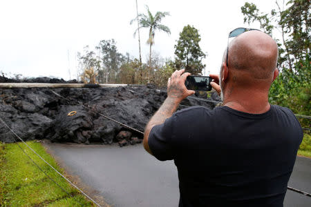 A resident of the Leilani Estates subdivision takes photos of a lava flow near his home during ongoing eruptions of the Kilauea Volcano, Hawaii, U.S., May 8, 2018. REUTERS/Terray Sylvester