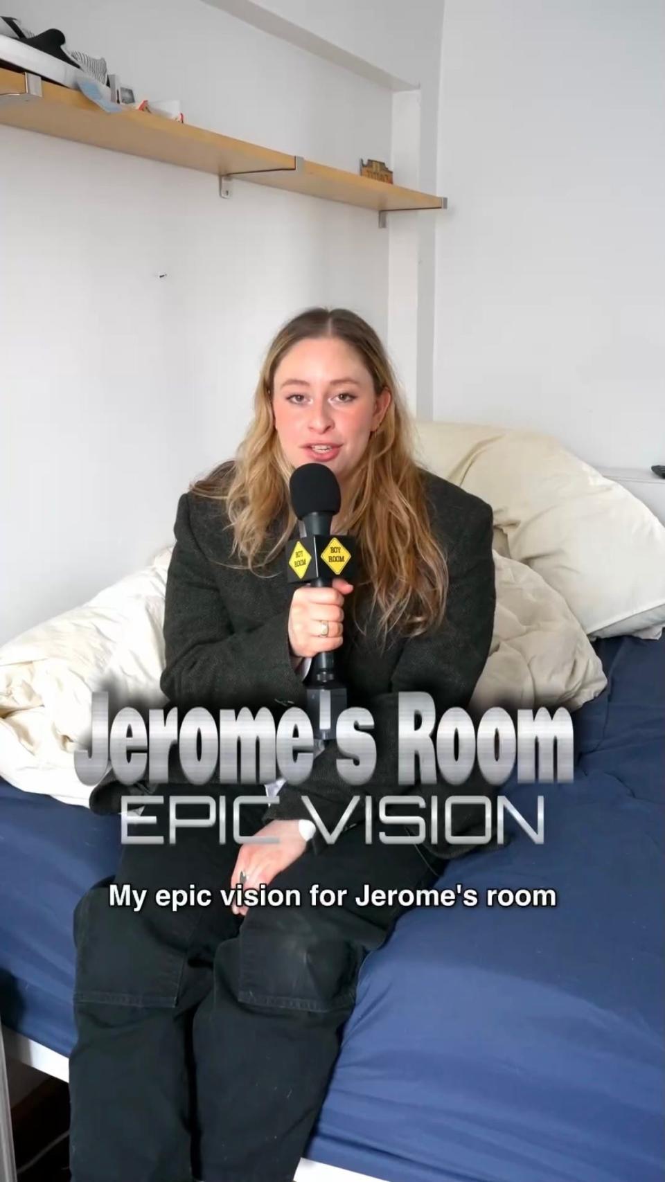 Rachel Coster sits on a bed wearing a black blazer and holding a microphone.