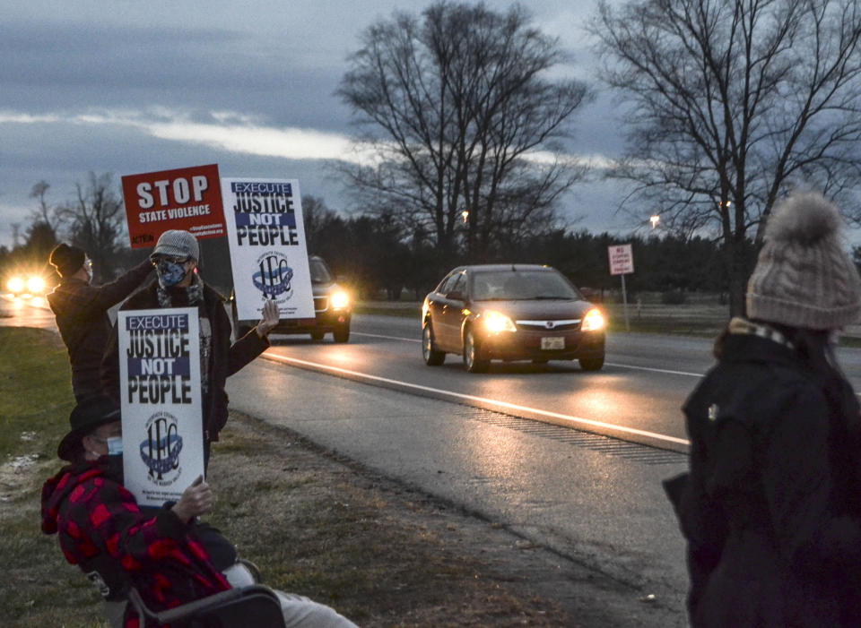 Protesters stand across Prairieton Road from the Federal Death Chamber Friday, Dec. 11, 2020 in Terre Haute, Ind. The Trump administration plans to continue its unprecedented series of post-election federal executions Friday by putting to death Alfred Bourgeois who severely abused his 2-year-old daughter for weeks in 2002, then killed her by slamming her head against a truck’s windows and dashboard.(Austen Leake/The Tribune-Star via AP)