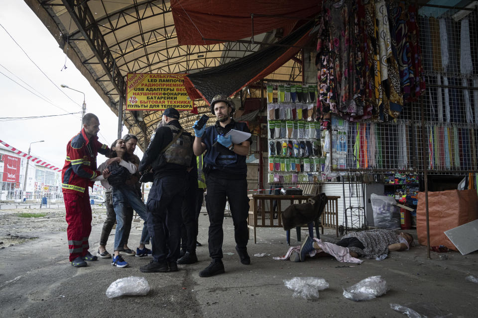 Sabina, second from left, cries as her husband Artem Pogorelets' body lies on the ground after he was killed by Russian shelling at Barabashovo market in Kharkiv, Ukraine, Thursday, July 21, 2022. (AP Photo/Evgeniy Maloletka)