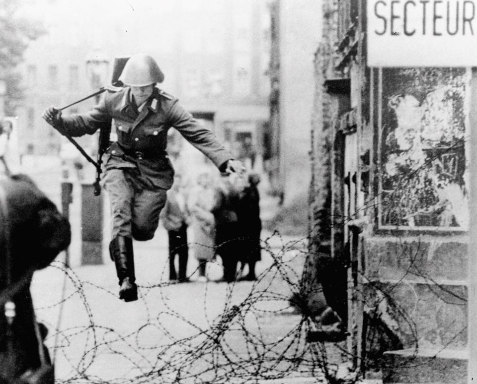 Defecting East German soldier leaps over a barbed wire barricade into West Berlin in 1961, before the wall went up.