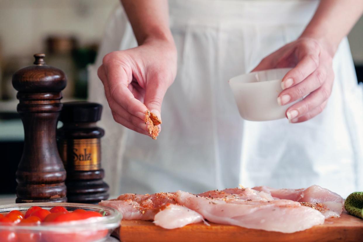 hands rubbing spices and salt on raw chicken