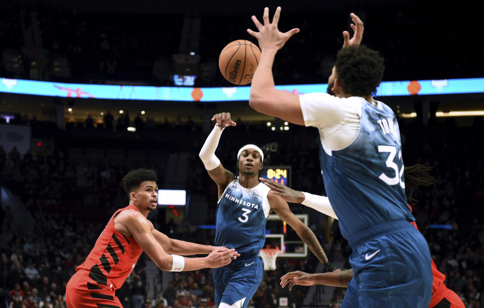 Minnesota Timberwolves forward Jaden McDaniels, center, passes the ball to center Karl-Anthony Towns, right, as Portland Trail Blazers forward Toumani Camara, left, defends during the first half of an NBA basketball game in Portland, Ore., Tuesday Feb. 13, 2024. (AP Photo/Steve Dykes)