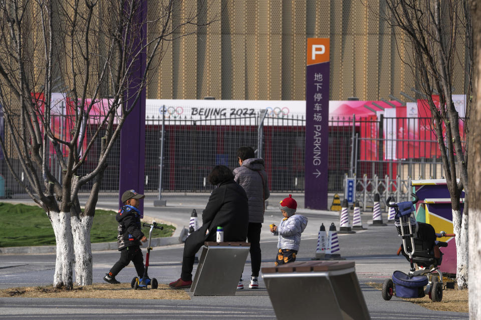 Residents bring their children play near a barricaded venue which host the men's and women's ice hockey games at the 2022 Winter Olympics in Beijing, Thursday, Feb. 10, 2022. The possibility of a large outbreak in the bubble, potentially sidelining athletes from competitions, has been a greater fear than any leakage into the rest of China. (AP Photo/Andy Wong)