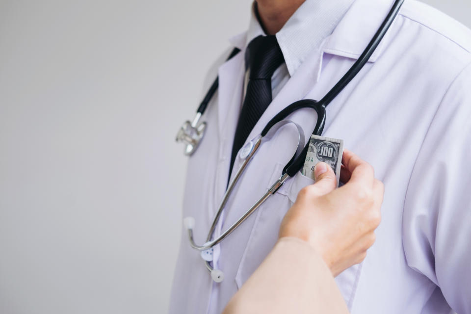 A person's hand places a hundred dollar bill in a doctor's shirt pocket.