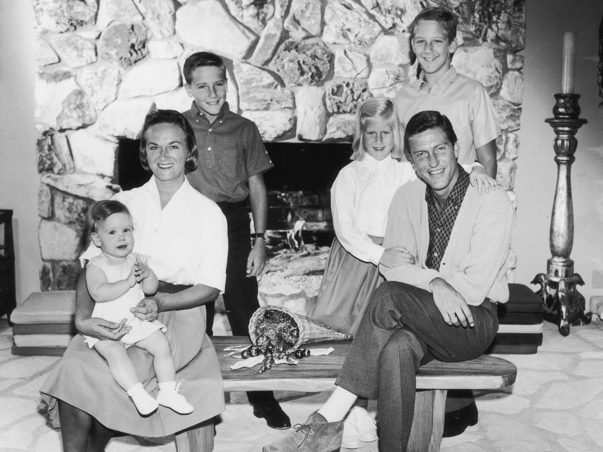 Dick Van Dyke with his wife, Margie Willet, posing in front of a fire place with their four children: Barry, Carrie, Chris, and Stacey. Van Dyke and Willet are sitting on a coffee table while their children stand behind them