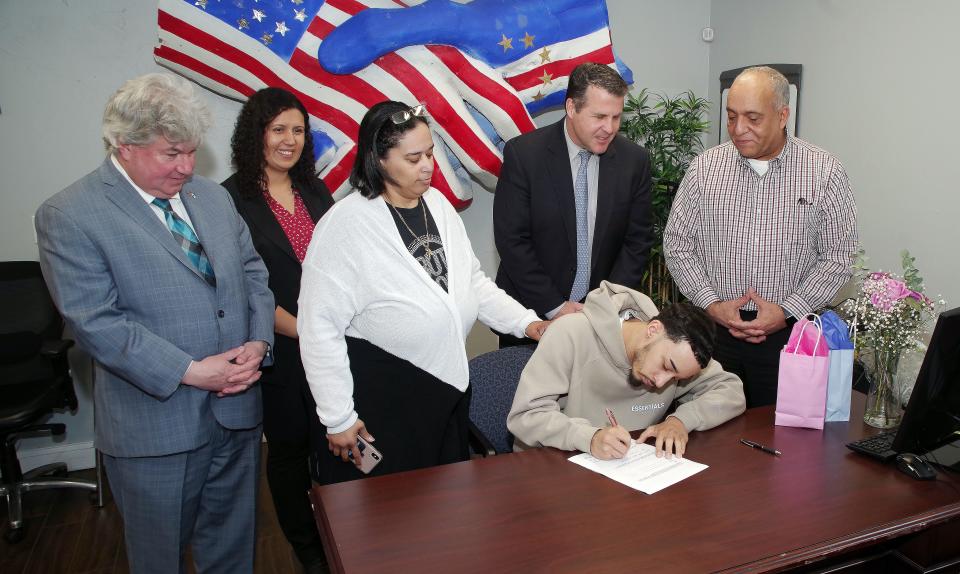 From left, state Sen. Michael Brady, of Brockton; Brockton City Councilor Rita Mendes; Nancy Demacedo-Fernandes; Brockton Mayor Robert Sullivan; and Councilor-at-large Moises Rodrigues look on as Nicalas Fenrandes signs his contract for an Olympic Scholarship on Monday, April 11, 2022, upon which he hopes to qualify for the 2024 Summer Olympics taekwondo competition being held in Paris.