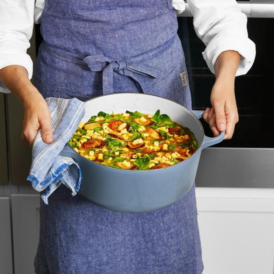 a person holding a gray pot of white bean sausage stew