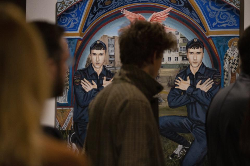 In this photo taken on Saturday, Oct. 26, 2019, visitors look at the works showing an extreme outsider's view of Moscow reality by self-taught painter Pasmur Rachuiko, in the Gogol Center in Moscow, Russia. Moscow’s suburbs are the focus of a major international art exhibition that has just opened in the Russian capital. The exhibit uses contemporary art to explore the many hidden facets of life beyond the Russian capital’s nucleus. Austrian cultural attache says the ‘real’ Moscow where most of the city’s 12.6 million people live, is outside the center. (AP Photo/Alexander Zemlianichenko)