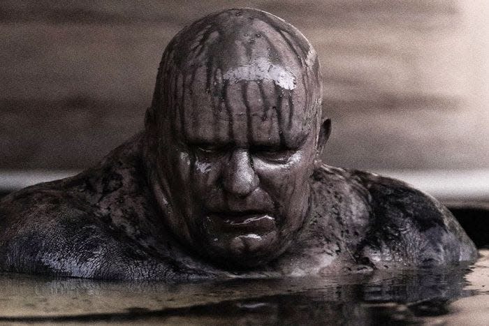 Stellan Skarsgard as Baron Vladimir Harkonnen in "Dune." A bald man covered in grey sludge rises from a pool of water.