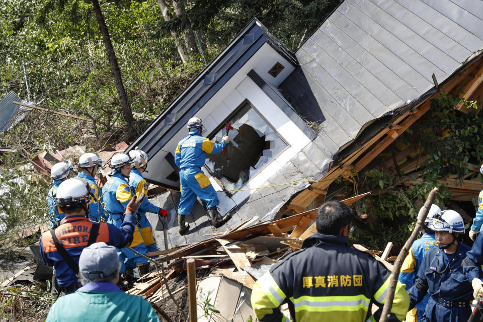 Police, in blue with yellow uniform, search for missing persons around a house destroyed by a landslide after a powerful earthquake in Atsuma town, Hokkaido, northern Japan, Thursday, Sept. 6, 2018. Several people were reported missing in the nearby the town, where a massive landslide engulfed homes in an avalanche of soil, rocks and timber. (Masanori Takei/Kyodo News via AP)