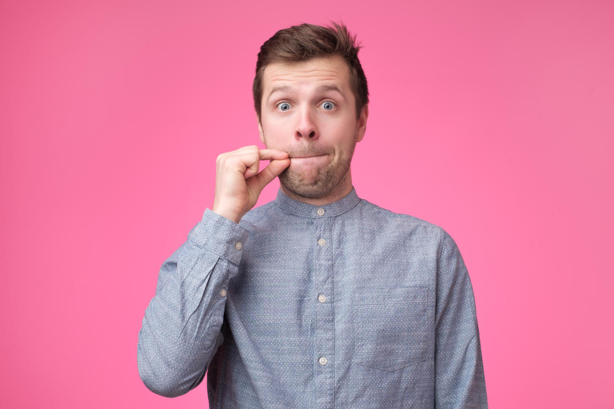 Young man showing a sign of closing mouth and silence gesture doing like closing his mouth with a zipper on isolated pink background