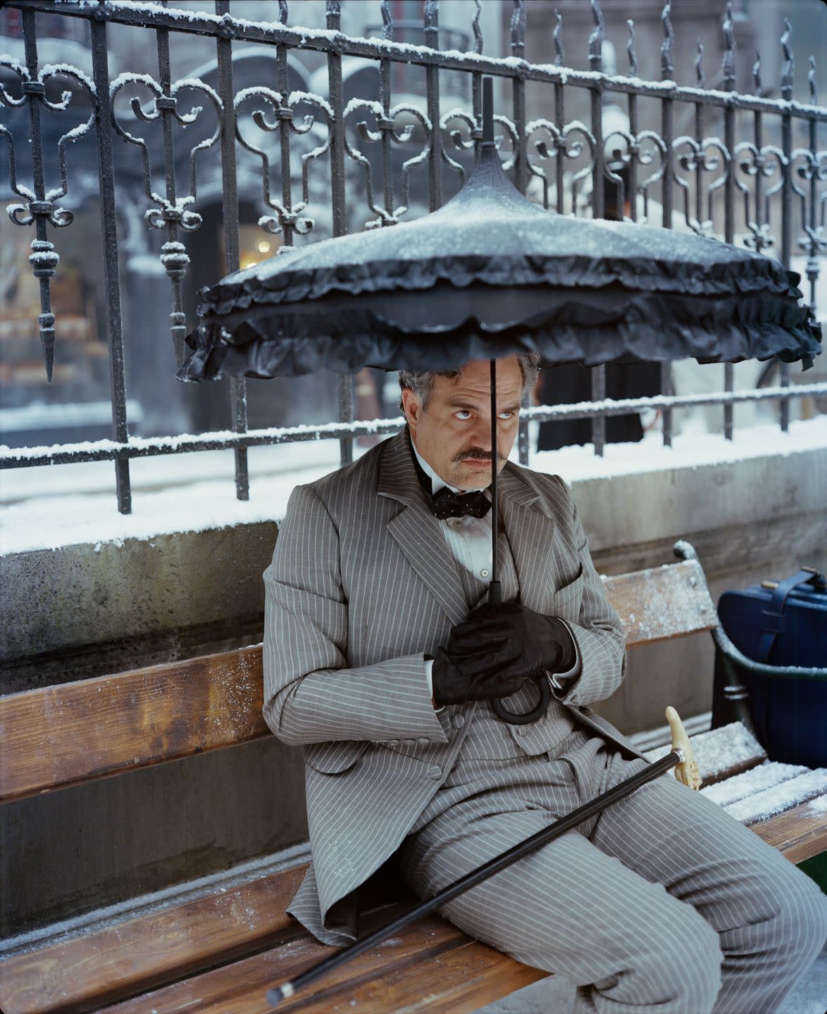 mark ruffalo sitting on a bench holding an umbrella in movie poor things