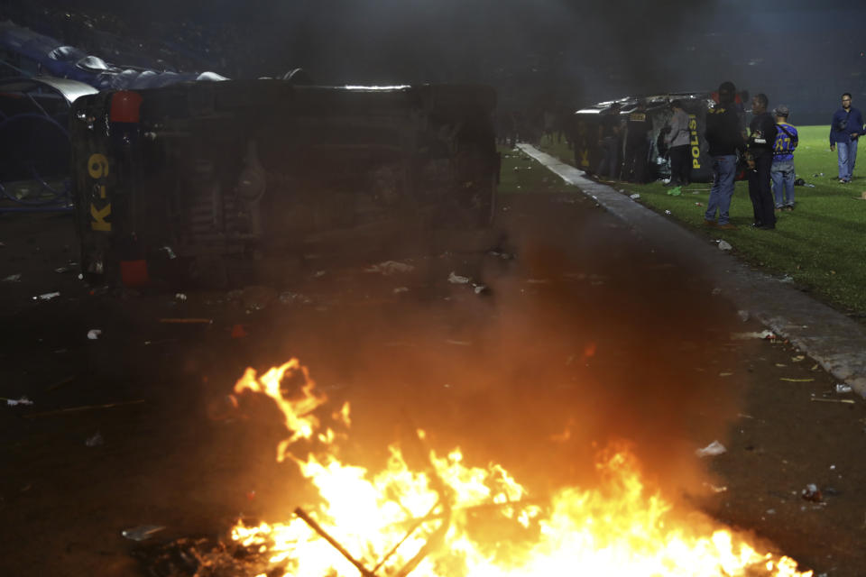 Plain-clothed officers stand near the wreckage of police vehicles damaged during a clash between supporters of two Indonesian soccer teams at Kanjuruhan Stadium in Malang, East Java, Indonesia, Saturday, Oct. 1, 2022. Panic following police actions left over 100 dead, mostly trampled to death, police said Sunday. (AP Photo/Yudha Prabowo)