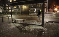 In this grab taken from video on Monday, Jan, 25, 2021, a person stands at a bus stop where the glass has been shattered after rioting, in Haarlem, Netherlands. Groups of youths have confronted police in several Dutch cities defying the country’s coronavirus curfew and throwing fireworks. Police in the port city of Rotterdam used a water cannon and tear gas in an attempt to disperse a crowd of rioters Monday night. (Mizzle Media via AP)