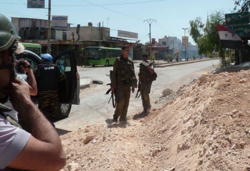 Syrian soldiers stand guard as smoke is seen in the background following a rocket-propelled grenade (RPG) attack near a team of UN truce observers during their visit to the Damascus suburb of Douma on May 20