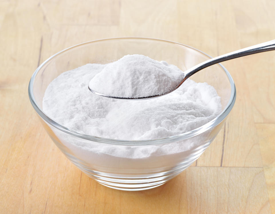 Close-up of baking soda on spoon against background of glass of water on wooden table. Bicarbonate of soda.