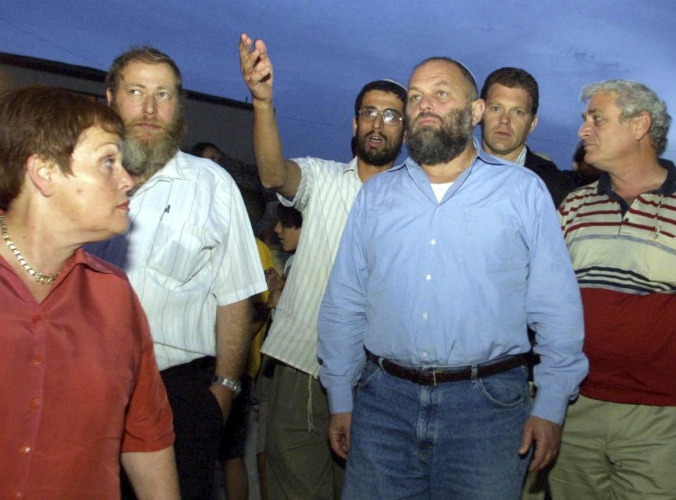 Israel's then-Infrastructure Minister Effie Eitam, center in blue shirt, listens to Jewish settlers when visiting Mitzpeh Assaf, an illegal outpost which Israel's Defense Minster said will be dismantled, near the settlement of Ofra, north of Jerusalem, Sunday Oct. 13, 2002. Israel plans to nominate Eitam to head the Yad Vashem Holocaust memorial, officials said Tuesday, Oct. 27, 2020. (AP Photo/Zoom 77)