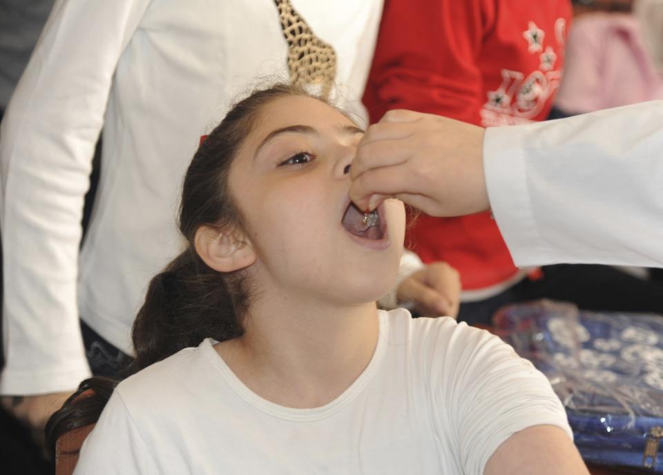 A Syrian health worker administers polio vaccination to a girl at a school in Damascus