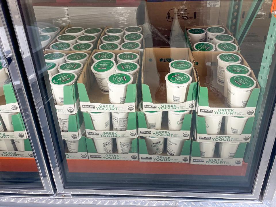 Containers of Greek yogurt with green lids in cardboard boxes in fridge at Costco