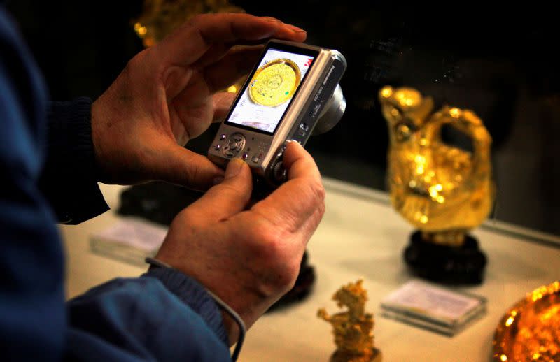 FILE PHOTO: A man takes a photo of gold miniature statues and plates on display at a Chinese cultural fair in Beijing