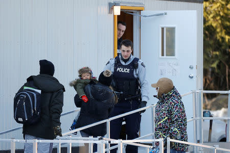 Royal Canadian Mounted Police (RCMP) officers look on as people enter a trailer after crossing the US-Canada border into Canada in Lacolle, Quebec, Canada., February 14, 2018. REUTERS/Chris Wattie