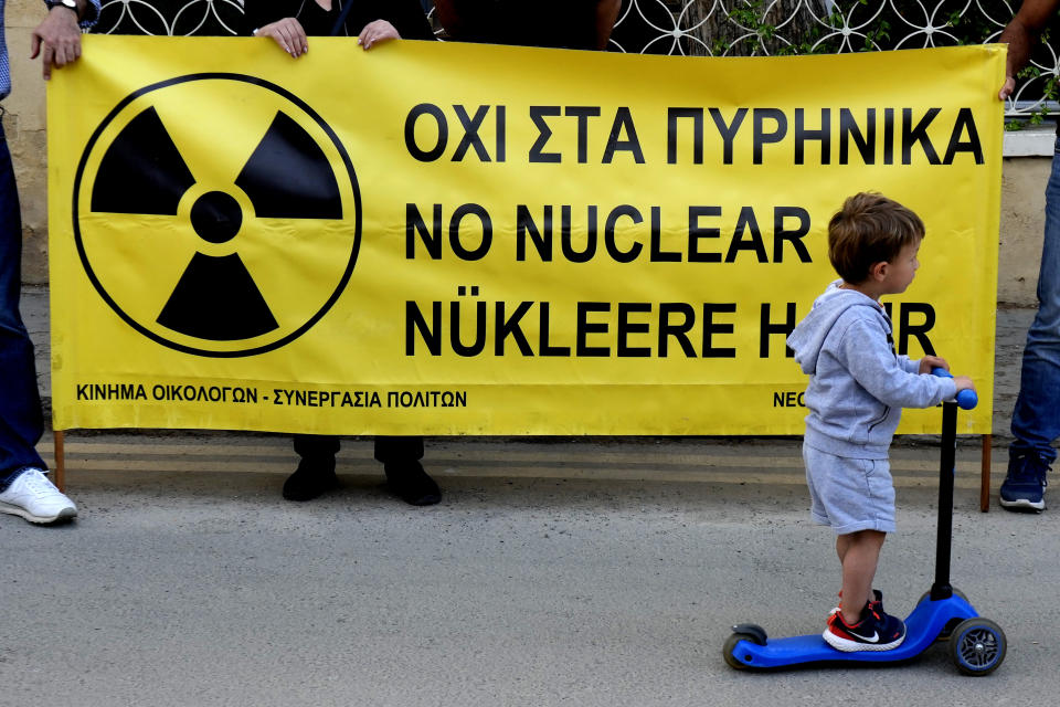 A boy with a scooter passes in front of an anti-nuclear banner during a protest with Greek and Turkish Cypriots activists voicing their unease over the ongoing construction of the Russian-owned Akkuyu nuclear power plant in southern Turkey, some 60 miles (100 km) from the island nation's northern coastline, inside the United Nations controlled buffer zone that cuts across the capital Nicosia, Cyprus, on Wednesday, April 27, 2022. Activists say uncertainty over the safety of war-wracked Ukraine's nuclear power plants has re-ignited concerns over a Russian-owned nuclear power plant that's currently being built in a quake-prone area on Turkey's southern coastline. (AP Photo/Petros Karadjias)