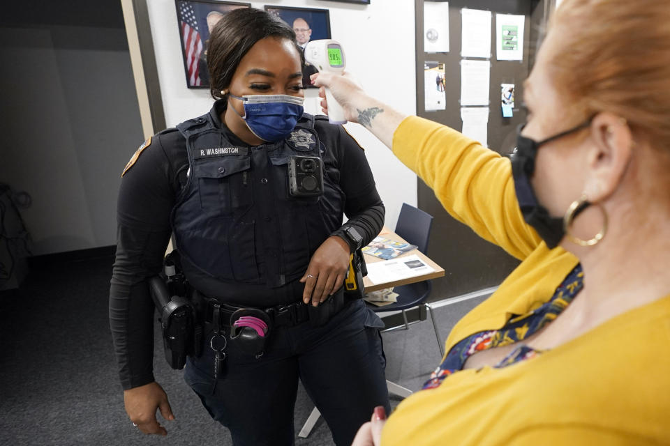 In this April 17, 2020, photo Harris County Sheriff's Deputy Ravin Washington, left, has her temperature checked by administrative assistant Kim Sumner before starting her patrol in Spring, Texas. Washington tested positive for COVID-19 in mid-March and returned to patrol on April 15 after recovering at home. (AP Photo/David J. Phillip)