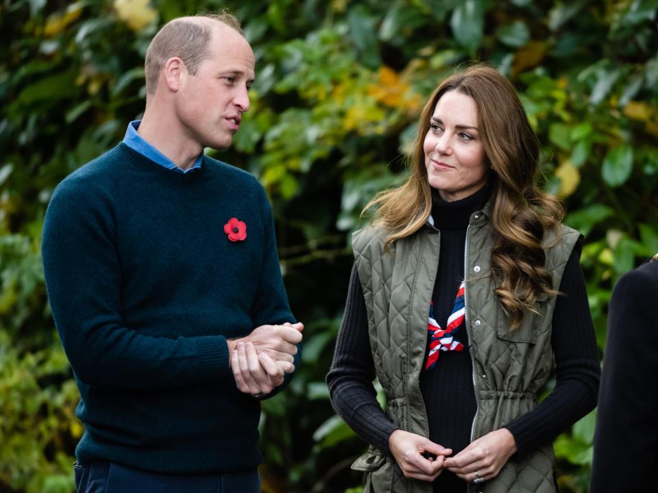 Kate Middleton stands next to Prince William and watches him speak in front of greenery