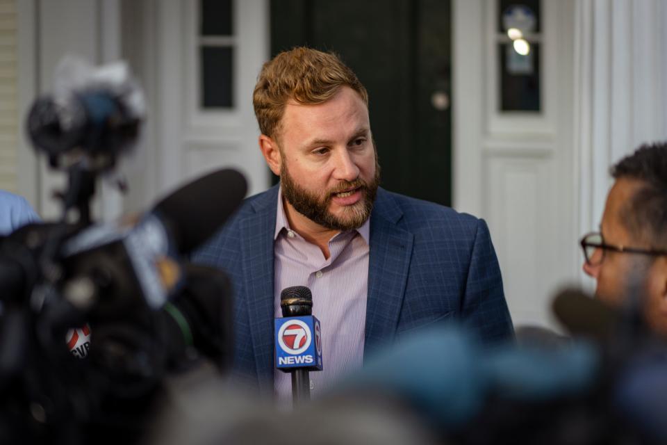 A man in a blazer speaks to reporters.